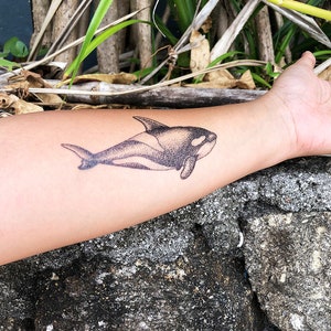 May include: A black and white temporary tattoo of an orca whale on a person's arm.