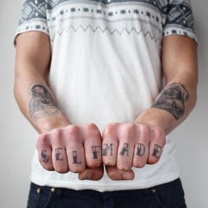 May include: A person's hands with temporary tattoos spelling out "SELF MADE" on their knuckles.