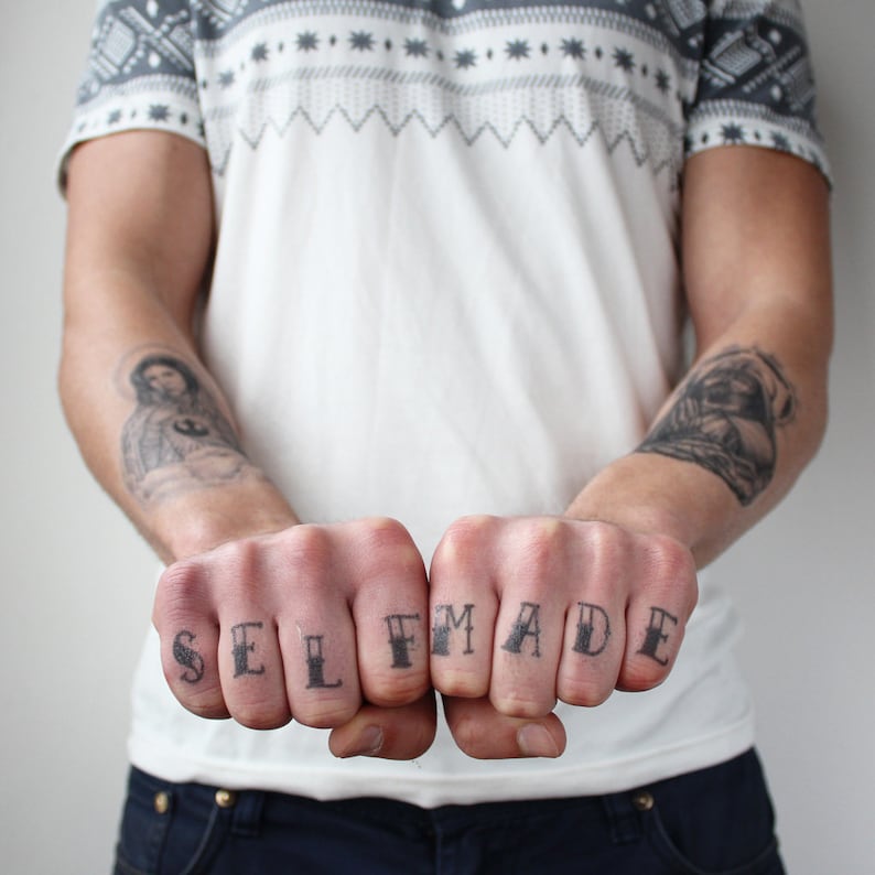 May include: A person's hands with temporary tattoos spelling out "SELF MADE" on their knuckles.