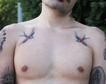 May include: A man with a tattoo of two blue, red, and black birds on his chest.