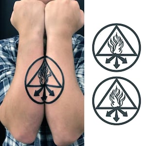 May include: Black tattoo design featuring a triangle with flames inside a circle, with three arrows pointing outwards. The design is on the forearm. Two identical designs are shown, one on each arm. The image also shows a plaid shirt.