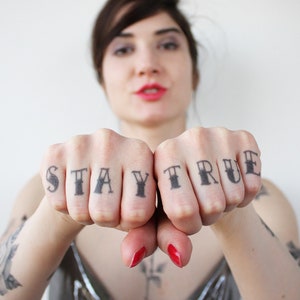 May include: A person's hands with the words "STAY TRUE" tattooed on their fingers.