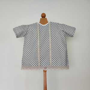 May include: A white dress with black polka dots and lace trim. The dress is on a wooden mannequin.