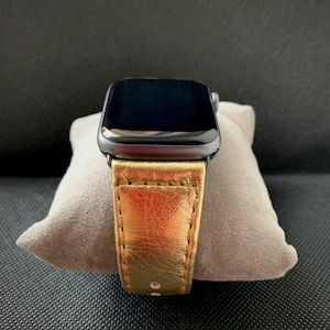 Może przedstawiać: Złoty skórzany pasek do zegarka z czarną tarczą Apple Watch.