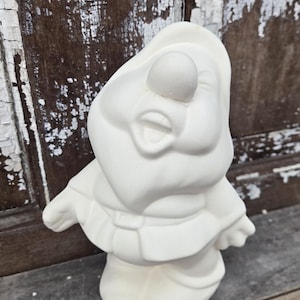 Könnte beinhalten: Eine weiße Keramik-Wichtelfigur mit großer Nase und Hut. Der Wichtel trägt eine Tunika und hat die Arme ausgestreckt. Die Figur ist unbemalt und bereit zur individuellen Gestaltung.