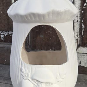 May include: A white ceramic mushroom-shaped planter with a large opening and a textured surface. The planter features a detailed relief of mushrooms and leaves on the front. The design is suitable for indoor or outdoor use.