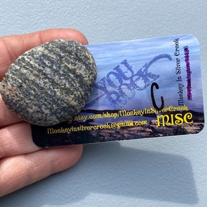 May include: A gray and black striped stone rests on a business card. The card features the text "YOU ROCK" and the shop name "Monkey In Silver Creek" with contact information.