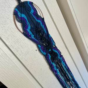 May include: A macrame wall hanging with a circular metal ring and blue, purple, and black yarn.