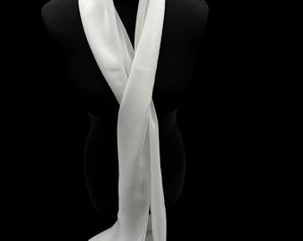 May include: A long, white scarf draped over a black mannequin. The scarf is made of a lightweight, flowing fabric, and it hangs in soft folds. The scarf is a solid, neutral color, and it appears to be made of silk or a similar material.