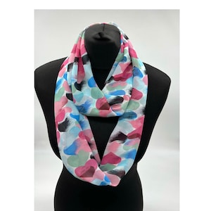 May include: A white infinity scarf with a colourful abstract print featuring pink, blue, green, and black brushstrokes.