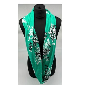 May include: A green infinity scarf with a white and black floral print.