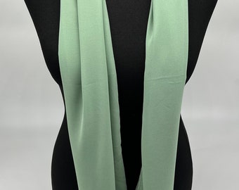 May include: A sage green scarf made of a soft, flowing fabric. The scarf is draped over a black mannequin.