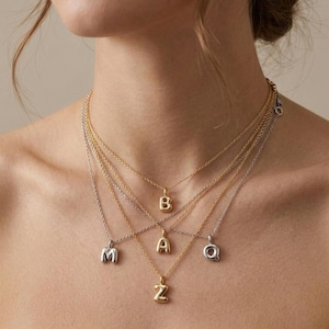 Puede incluir: Una colecci&oacute;n de collares con iniciales en oro y plata. Cada collar presenta un colgante con una sola letra, incluyendo las letras M, B, A, Z y Q. Los collares se muestran en el cuello de una persona, mostrando los diferentes estilos y colores.