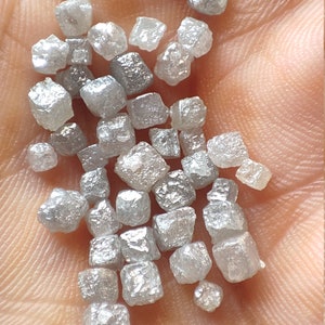 Puede incluir: Una colección de pequeños diamantes grises en bruto. Los diamantes son de diferentes tamaños y formas, pero todos son aproximadamente cúbicos.