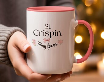 May include: White ceramic mug with a pink interior and handle. The mug features the text "St. Crispin Pray for us" in black script, with floral and bow accents. A perfect gift for any occasion.