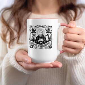 May include: White ceramic mug with a pink interior and handle. The mug features a black and white illustration of a religious figure with the text "LORD, MAKE ME AN INSTRUMENT". The design includes birds, deer, and a fox.