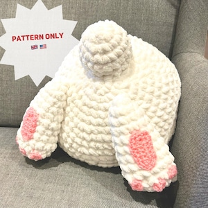 May include: White crocheted bunny plush toy with pink paw pads. The bunny is sitting on a gray fabric surface.