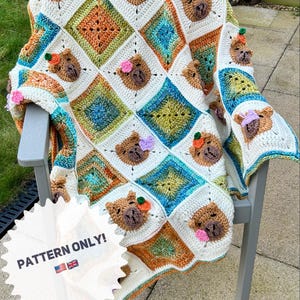 May include: A crochet baby blanket with a white background and colorful squares featuring brown bear faces. The blanket is draped over a chair with the text "PATTERN ONLY!" on a white starburst.