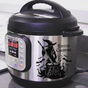 May include: A stainless steel Instant Pot electric pressure cooker with a black and white decal of a witch stirring a cauldron with bats flying around it. The decal reads "Electric Cauldron".