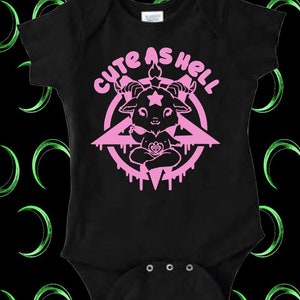 May include: Black baby onesie with a pink pentagram and a cute pink goat inside. The text "Cute as Hell" is written in a pink bubble font around the pentagram.