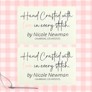 Może przedstawiać: Dwie kremowe etykiety z napisem "Hand Crafted with love in every stitch" elegancką czcionką. Poniżej napis "by Nicole Newman, CALABASAS, LOS ANGELES." Igła i nić znajdują się w lewym dolnym rogu.