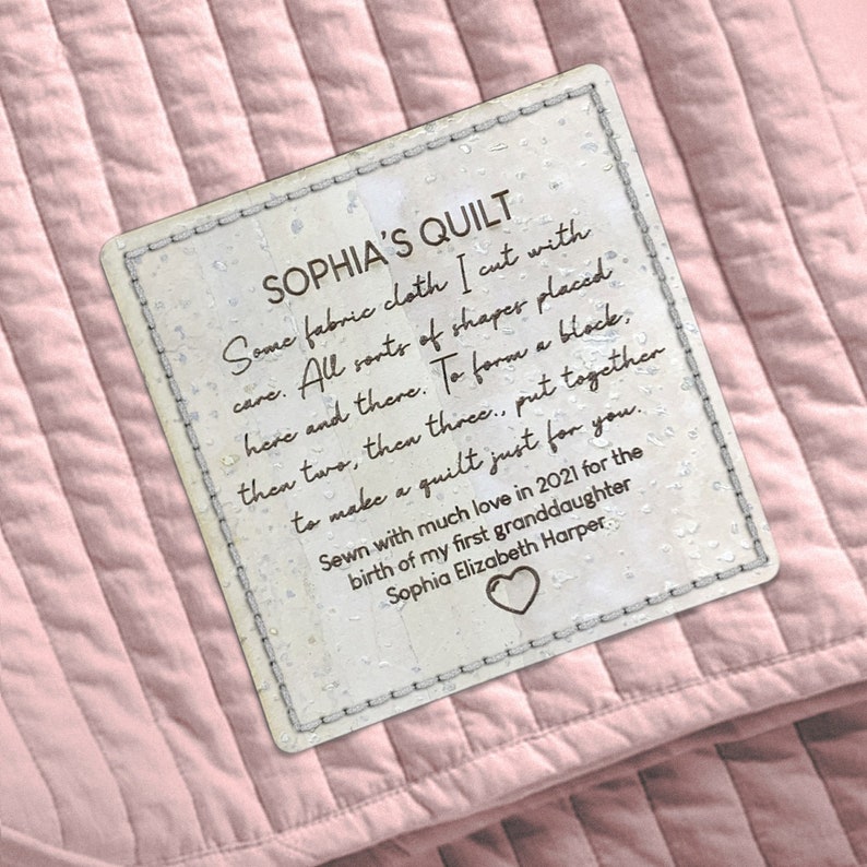 May include: A white tag with brown text that reads "Sophia's Quilt" and describes the quilt's creation. The tag is sewn onto a pink quilted fabric.