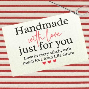 Może przedstawiać: Biała prostokątna etykieta z napisem "Handmade with Love just for you" w czarnym i różowym kolorze. Etykieta znajduje się na czerwono-białym pasiastym materiale, z igłą i nicią.