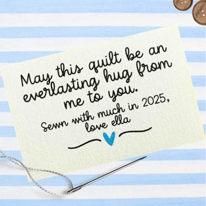 Puede incluir: Una etiqueta de tela color crema con texto negro: "Que este edredón sea un abrazo eterno de mí para ti. Cosido con mucho en 2025, love ella." También se ven un corazón azul y una aguja con hilo.