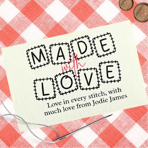 Może przedstawiać: Kremowa etykieta z napisem "MADE with LOVE" czarnymi, blokowymi literami. Słowa "with" i "LOVE" są pisane kursywą. Etykieta zawiera również tekst "Love in every stitch, with much love from Jodie James."