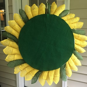 May include: A burlap sunflower wreath with yellow and green petals. The wreath has a green felt backing.