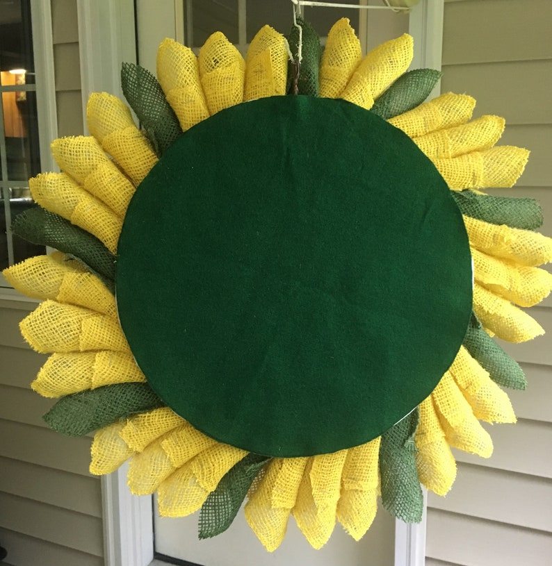 May include: A burlap sunflower wreath with yellow and green petals. The wreath has a green felt backing.