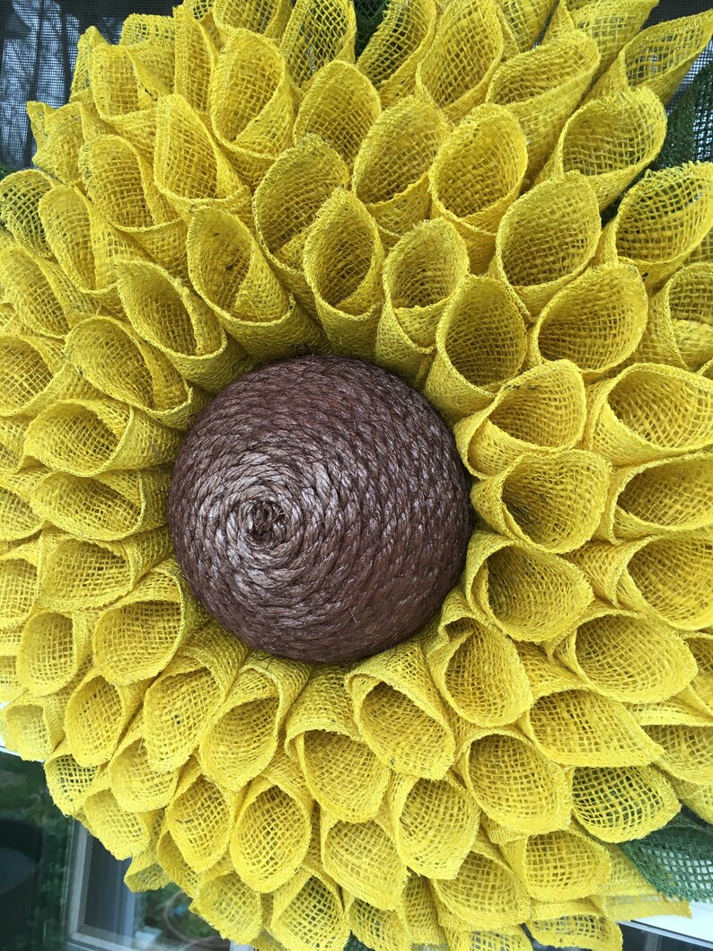 May include: A yellow burlap sunflower wreath with a brown burlap centre. The wreath is made of multiple layers of burlap, creating a full and fluffy look.