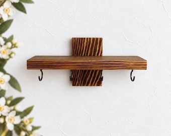 May include: A wall-mounted wooden shelf featuring a dark brown stained finish with a visible wood grain pattern. The shelf includes a vertical back support piece and four small, curved metal hooks attached to the underside for hanging items.