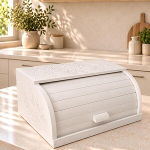 Peut inclure: Une boîte à pain en bois blanc avec une porte coulissante et une petite poignée rectangulaire. Le dessus et les panneaux latéraux présentent des motifs circulaires en relief de style mandala. La boîte a une base rectangulaire.