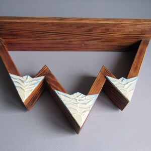 May include: A wooden shelf with a triangular design. The shelf has three tiers and is painted in a light brown color. The front of each tier is painted white with a textured design.