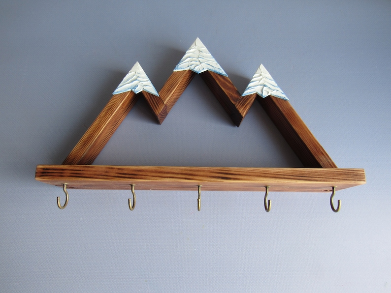 May include: Wooden mountain-shaped shelf with five hooks underneath. The shelf is stained brown and has white painted peaks.