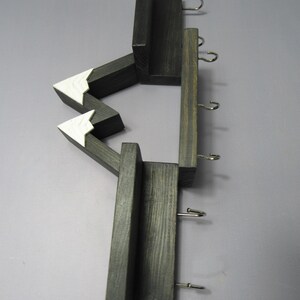 May include: A wall-mounted wooden organizer featuring a dark charcoal finish with two white-painted triangular mountain peaks. The structure includes multiple horizontal shelves and five silver-toned metal hooks for hanging items in a vertical arrangement.