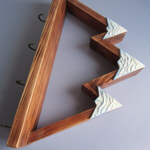 May include: Wooden key holder shaped like a mountain range with three hooks. The mountain peaks are painted white with blue accents.