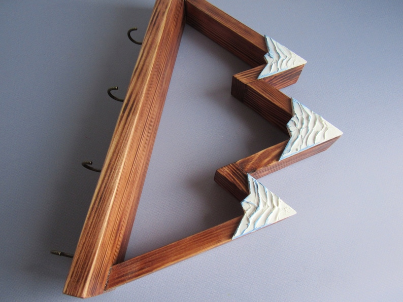 May include: Wooden key holder shaped like a mountain range with three hooks. The mountain peaks are painted white with blue accents.