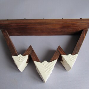 May include: A wall-mounted shelf featuring a dark brown stained wooden frame with a zigzag design. The three downward-pointing triangular peaks are finished with a thick, textured white paint, creating a mountain-like appearance on the lower edge.