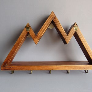 May include: A wooden wall shelf shaped like a mountain range with five hooks on the bottom. The shelf is stained a dark brown color.