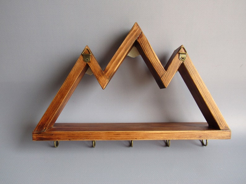 May include: A wooden wall shelf shaped like a mountain range with five hooks on the bottom. The shelf is stained a dark brown color.