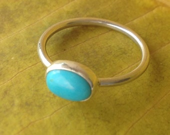 Op de afbeelding: Een zilveren ring met een turquoise ovale edelsteen. De ring ligt op een geel blad.
