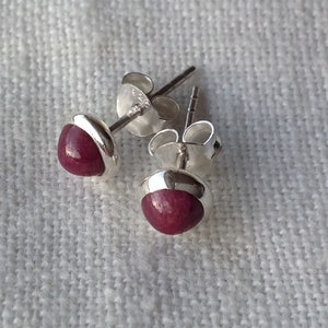 Könnte beinhalten: Ein Paar silberne Ohrstecker mit jeweils einem tief roten Edelstein. Die Ohrringe sind schlicht und elegant.