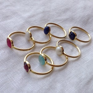 Può includere: Un set di sei anelli d'oro con pietre preziose di diversi colori. Gli anelli presentano una varietà di pietre, tra cui un rubino, una perla, una turchese e un lapislazzuli.