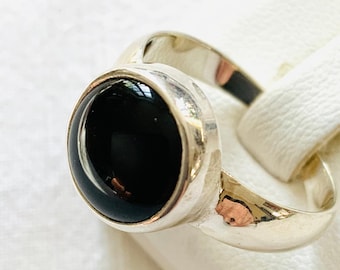 May include: A silver ring with a black oval gemstone. The ring is set on a white background.