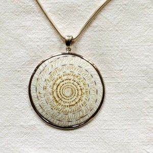 Peut inclure: Un collier en chaîne argent avec un pendentif rond orné d'un motif de coquille en spirale blanche et brune.