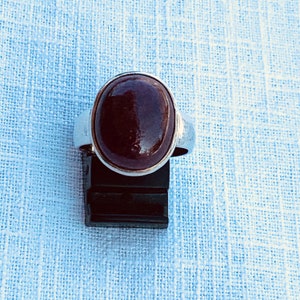 Op de afbeelding: Een zilveren ring met een grote, ovale, donkerrode edelsteen.