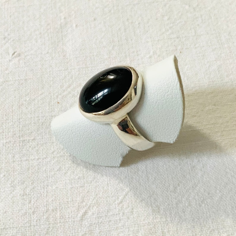 Op de afbeelding: Een zilveren ring met een zwarte ovale edelsteen. De ring ligt op een witte displaystandaard.