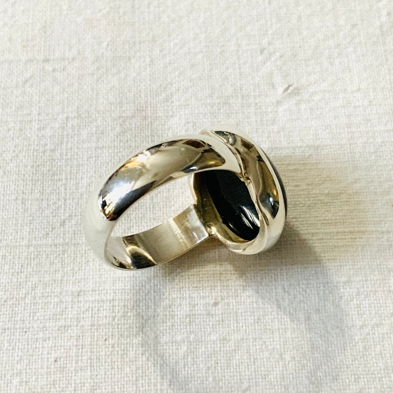 Op de afbeelding: Een zilveren ring met een zwarte ovale edelsteen. De ring is in een eenvoudige, elegante stijl.